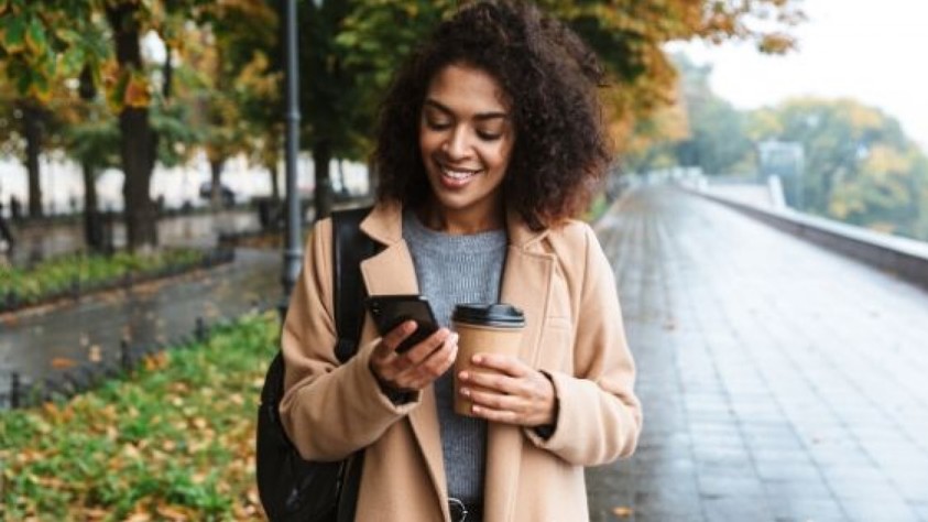 Person outside on a wet day looking at her phone while holding a paper cup.